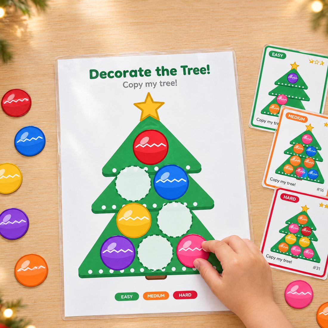 A child's hand placing a pink ornament on the printed Christmas tree mat, with challenge cards beside it